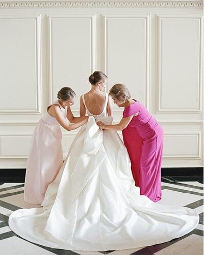 Photo of bridemaids helping bride with dress