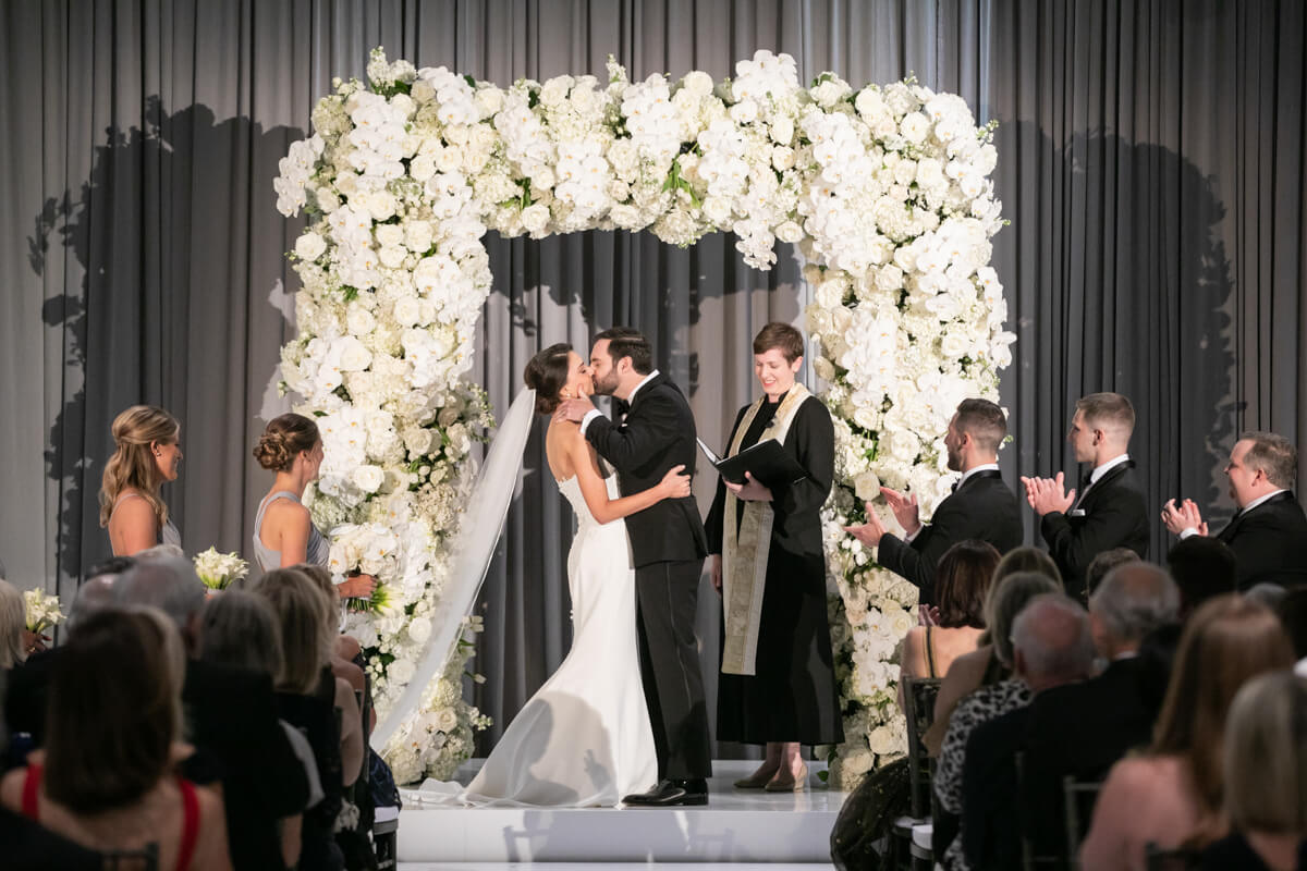 carey and david kissing under white floral arch