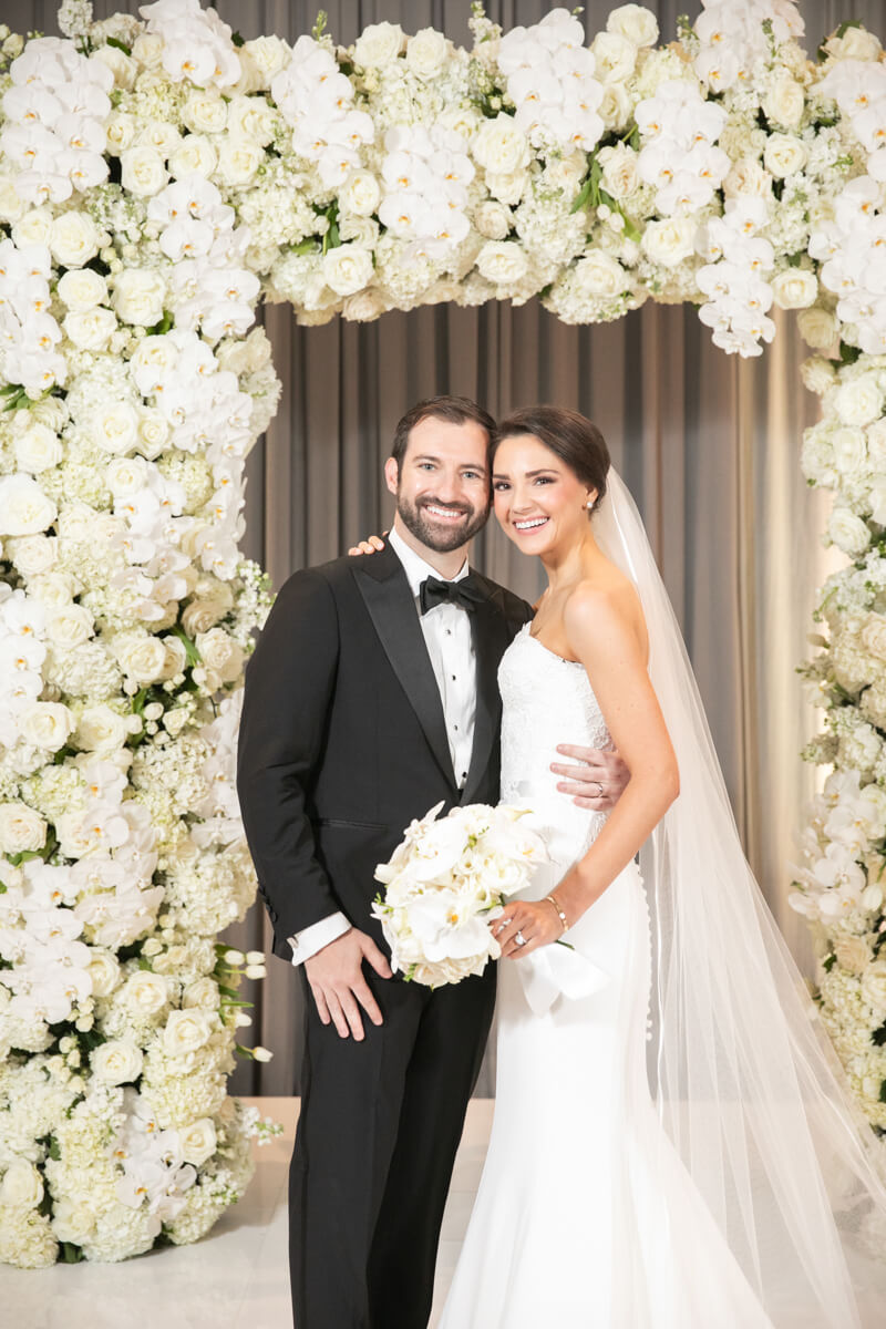 carey and david in front of white floral arch