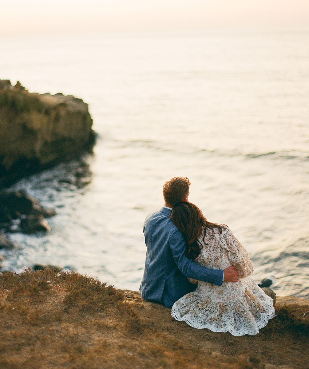 Bride and groom sitting on cliff looking over seaside